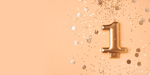 Gold candle in the form of number one on peach background with confetti and bokeh lights.