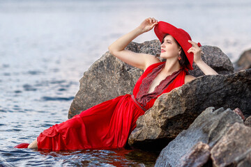 A beautiful elegant lady in a red hat and a long red dress is swimming in the water near the...