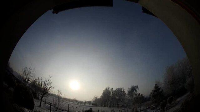 Window view with sky. One day from sunrise to sunset with moving clouds, sun all day low on horizon. Horizon with snow, trees and car traffic on two-lane road - timelapse, panorama 204. 