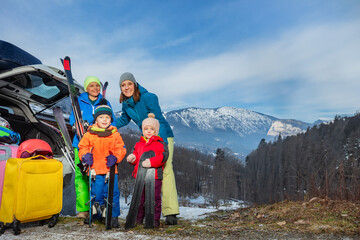 Mother at vacation stand holding ski by car arrived with 3 kids
