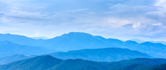 Landscape of mountain range in cool tone blue color at sunrise with morning fog and cloudy sky. Mountain peak in rainy season.