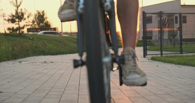 Man casual wear rides folding bicycle to camera, sidewalk, front view, sunset, sky, urban danger