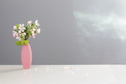 branches of  apple tree with flowers in pink vase on white table