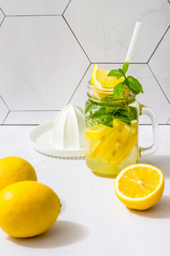 A glass with refreshing lemonade and mint, the process of preparing a drink, a citrus juicer and limines with mint on a light background.
