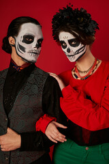scary couple in catrina calavera makeup looking at camera on red, dia de los muertos tradition