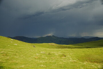 Paisaje de pradera verde bajo un cielo oscuro de tormenta con lluvia cayendo sobre las montañas. © felix