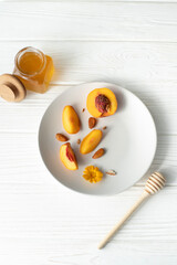 A plate with an apricot, honey and a honey spoon on a white background