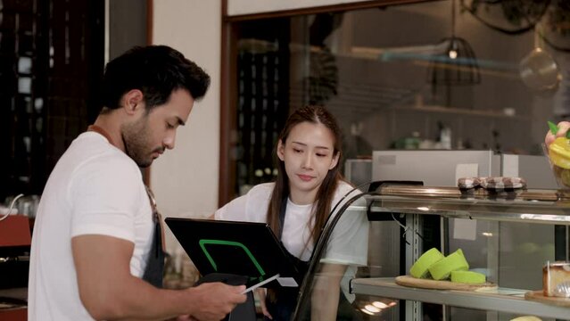 Unrecognizable face employee man checking bakery stock using tablet, Hispanic husband and Asian wife working together receive online orders by technology application in cafe coffee shop or restaurant
