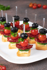 Canape with cherry tomatoes, sausage, cheese and black olives on white plate, Close up