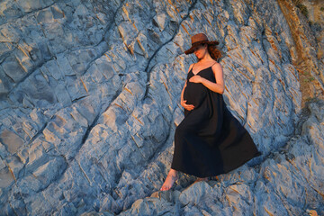 young pregnant woman in a dress goes down the rock to the seashore