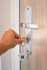 Hand unlocking the door with a key with a small house pendant. Photo suitable for real estate...