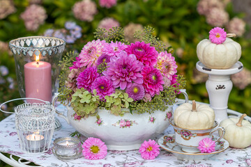 romantisches Arrangement mit Blumengesteck mit pink Dahlien, weißen Kürbissen und Windlichtern