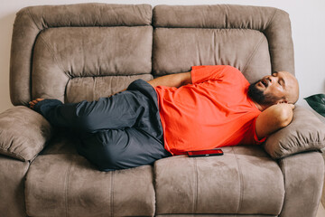Fat and bald man laying on the couch taking a nap