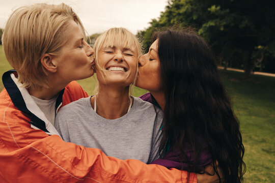 Two women kissing their friend on the cheeks outdoors
