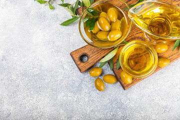 Olive oil in glass bowls, gravy boats and bottle on a textured kitchen table. Oil bottle with branches and fruits of olives. Place for text. copy space. cooking oil and salad dressing.Close-up.Flatley