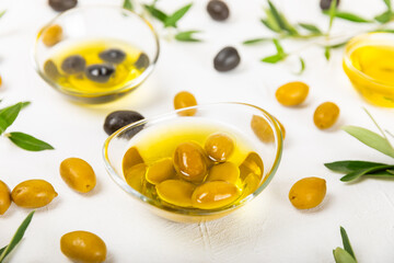 Olive oil in glass bowls, gravy boats and bottle on a textured kitchen table. Oil bottle with branches and fruits of olives. Place for text. copy space. cooking oil and salad dressing.Close-up.Flatley