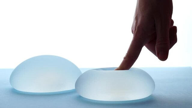 Woman pressing soft round breast implant in backlight. Plastic surgery