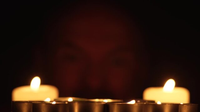 Burning candles with Mentally ill scary man grimaces looking into camera on background. Blurred terrible male portrait. Horror fear voodoo witchcraft magic
