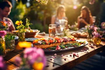Fotobehang Grupo de amigos almorzando en una hermosa mesa en el jardín. Concepto de estilo de vida. Comida y bebida en el exterior disfrutando de una fiesta en el restaurante. © TaniaC.