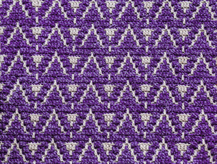 Abstract knitted background. Purple white crochet texture with mosaic pattern.