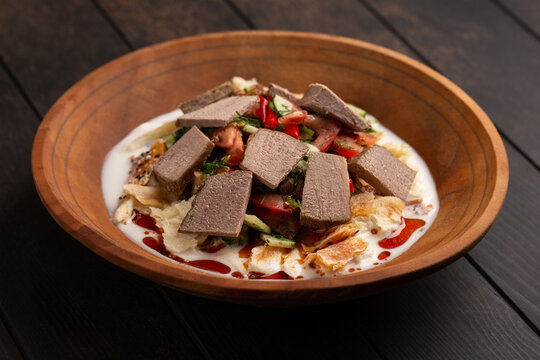 Traditional tajik dish - kurutob or qurotob with sour milk, fatir bread, vegetables and beef in a wooden bowl on wooden background closep.Tajikistan food.