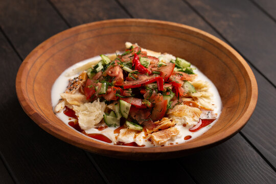 Traditional tajik dish - kurutob or qurotob with sour milk, fatir bread and vegetables in a wooden bowl on wooden background closep.Tajikistan food.