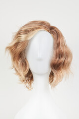 Natural looking blonde fair wig on white mannequin head. Short hair cut on the plastic wig holder isolated on white background, front view.