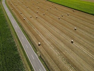 Fototapeta premium Aerial view of a landscape with a road between a cornfield and a grass field with hay bales 