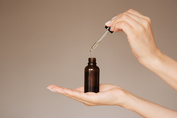 human's hand holds a dark bottle of cosmetic liquid and drips into it with a pipette. isolated on a light background