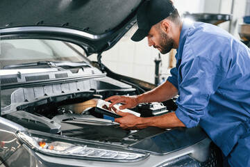 Using tablet. Auto mechanic working in garage. Repair service