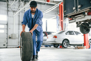 Fototapeta premium Walking forward with new tire. Auto mechanic working in garage. Repair service
