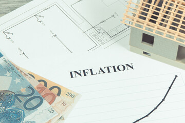 Inscription inflation, currencies Euro, toy house under construction and construction drawings. High prices of real estate, building or rent home