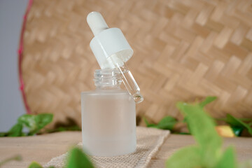 Glass dropper bottle with a white rubber dropper tip and leaves on a beautiful woven bamboo background. Serum dropper bottle. Aromatherapy eyedropper jar. Cosmetic Serum. Trendy nature concept.