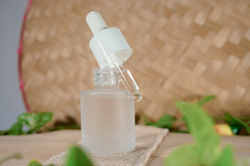 Glass dropper bottle with a white rubber dropper tip and leaves on a beautiful woven bamboo background. Serum dropper bottle. Aromatherapy eyedropper jar. Cosmetic Serum. Trendy nature concept.