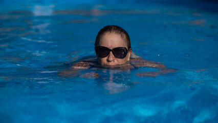 An elderly woman in sunglasses swims in the pool. Vacation in retirement. 