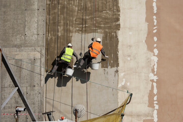 Workers paints the building wall. Painters hanging on a cables with paint buckets, steeplejack...
