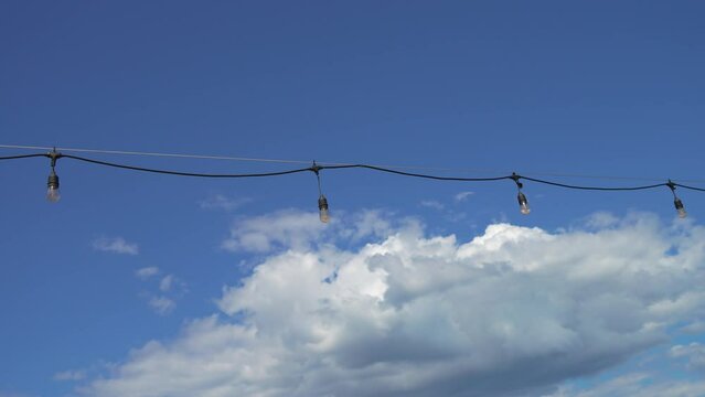 Electric wire with halogen bulbs on blue sky background. Retro style. Vintage decoration for wedding or birthday celebration