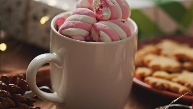 Pastel Christmas decoration on the table with flickering bulbs and hot drink with marshmallow