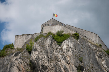 Tourist attraction museum Citadelle de Dinant in Belgium mountaintop fortress in historic Ardennes. Medieval fortified barracks with national flag overlooks city and river on sunny summer day