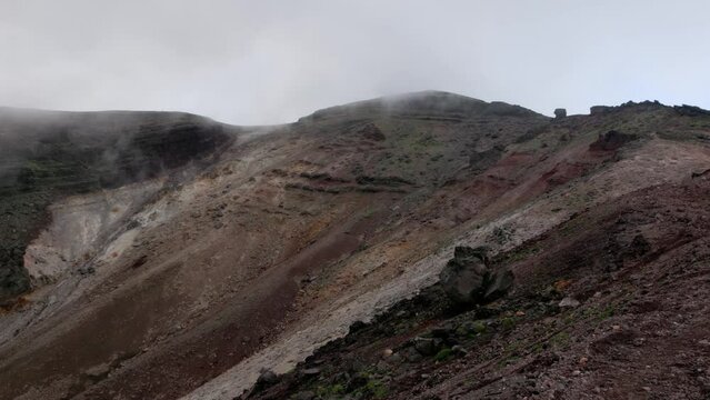 Handheld steep rocky slope of volcanic mountain summit in fog and mist