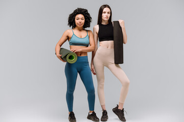 Females with exercise mat standing together isolated on gray copy space background