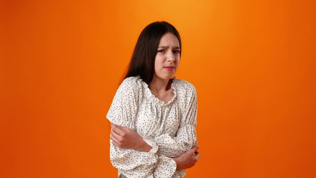 Teen girl suffering stomach ache against orange background in studio