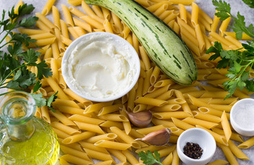 Food background. Penne pasta, zucchini, cream cheese, olive oil, parsley, garlic, salt and black pepper, top view. Ingredients for making vegetarian pasta
