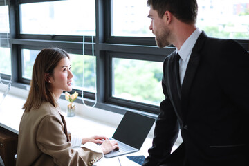 Beautiful asian secretary discussing problems with her handsome caucasian boss in the modern workspace.