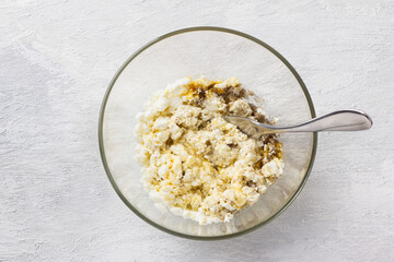 Glass bowl with mixed cottage cheese, eggs and vanilla sugar on a light gray background, top view. Cooking stage