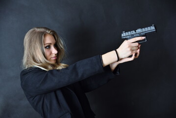 Charming young woman with blonde hairs and blue eyes, black background. Female model with gun in her hands. - obrazy, fototapety, plakaty