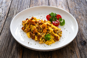 Scrambled eggs with chanterelle mushrooms with fresh tomato salad on wooden table
