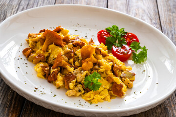 Scrambled eggs with chanterelle mushrooms with fresh tomato salad on wooden table
