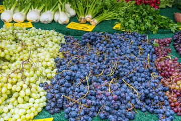 Red and white grapes with some vegetables for sale at a market