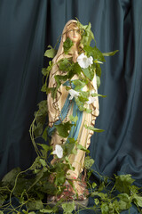 a statuette of the Virgin Mary covered with bindweed in front of a wavy green curtain